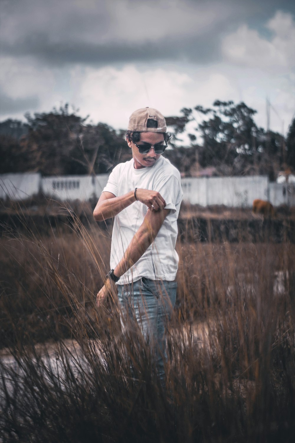 man in white t-shirt, brown snapback cap, and blue jeans