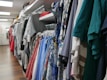 A variety of colorful clothes hang neatly on racks in a well-organized retail store. The garments include shirts, dresses, and jackets in different patterns and colors, filling the space with a vibrant and inviting atmosphere.