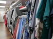 A variety of colorful clothes hang neatly on racks in a well-organized retail store. The garments include shirts, dresses, and jackets in different patterns and colors, filling the space with a vibrant and inviting atmosphere.