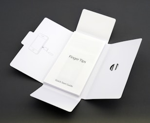A Quick Start Guide titled 'Finger Tips' is placed in the center of an unfolded white cardboard package. The right side of the package has a cut-out opening, and the left side shows an illustration of a phone and a tool.