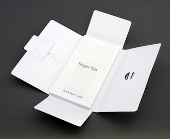 A Quick Start Guide titled 'Finger Tips' is placed in the center of an unfolded white cardboard package. The right side of the package has a cut-out opening, and the left side shows an illustration of a phone and a tool.