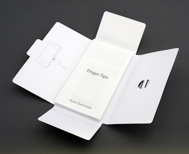 A Quick Start Guide titled 'Finger Tips' is placed in the center of an unfolded white cardboard package. The right side of the package has a cut-out opening, and the left side shows an illustration of a phone and a tool.