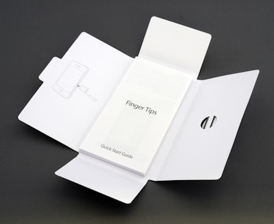 A Quick Start Guide titled 'Finger Tips' is placed in the center of an unfolded white cardboard package. The right side of the package has a cut-out opening, and the left side shows an illustration of a phone and a tool.