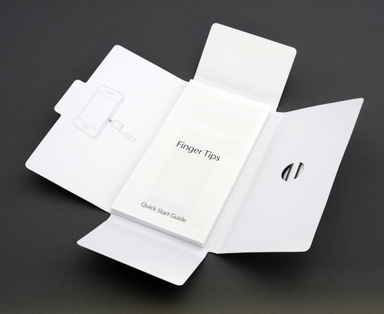 A Quick Start Guide titled 'Finger Tips' is placed in the center of an unfolded white cardboard package. The right side of the package has a cut-out opening, and the left side shows an illustration of a phone and a tool.