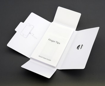 A Quick Start Guide titled 'Finger Tips' is placed in the center of an unfolded white cardboard package. The right side of the package has a cut-out opening, and the left side shows an illustration of a phone and a tool.
