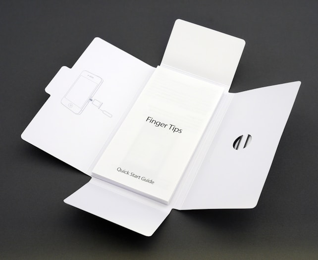 A Quick Start Guide titled 'Finger Tips' is placed in the center of an unfolded white cardboard package. The right side of the package has a cut-out opening, and the left side shows an illustration of a phone and a tool.