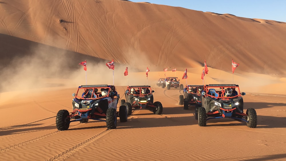 three red monster trucks on sand dunes