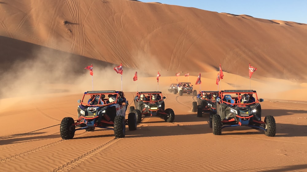 Trois monster trucks rouges sur des dunes de sable