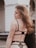 A young woman with long, wavy hair is seen from the back. She is wearing black lingerie with sheer, polka dot details. The background is urban, featuring an archway and a railing with a blurred car and building.