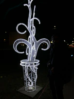 Side view of the 'Projekt Ayame' sculpture glowing with vibrant neon accents against a dark background.