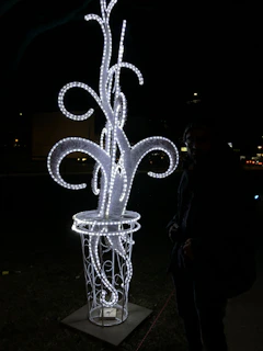 Side view of the 'Projekt Ayame' sculpture glowing with vibrant neon accents against a dark background.