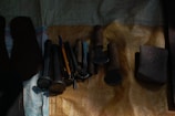 A collection of various tools laid out on a textured surface. The tools appear to include hammers, files, and chisels with wooden handles, alongside a pen and a stone object. The surface is covered with a woven material of varying shades.