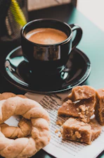 Close-up of a steaming cup of coffee beside a flaky sausage roll on a rustic plate.