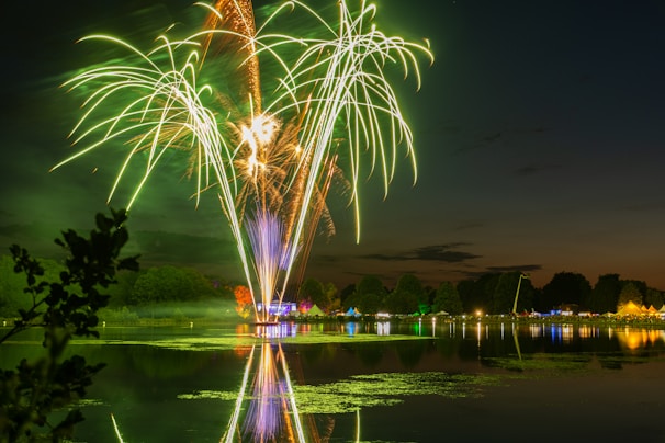 Colorful firework shells launching into the sky from a lakeside