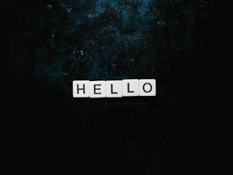 White square tiles spell out the word 'HELLO' against a dark, textured background.