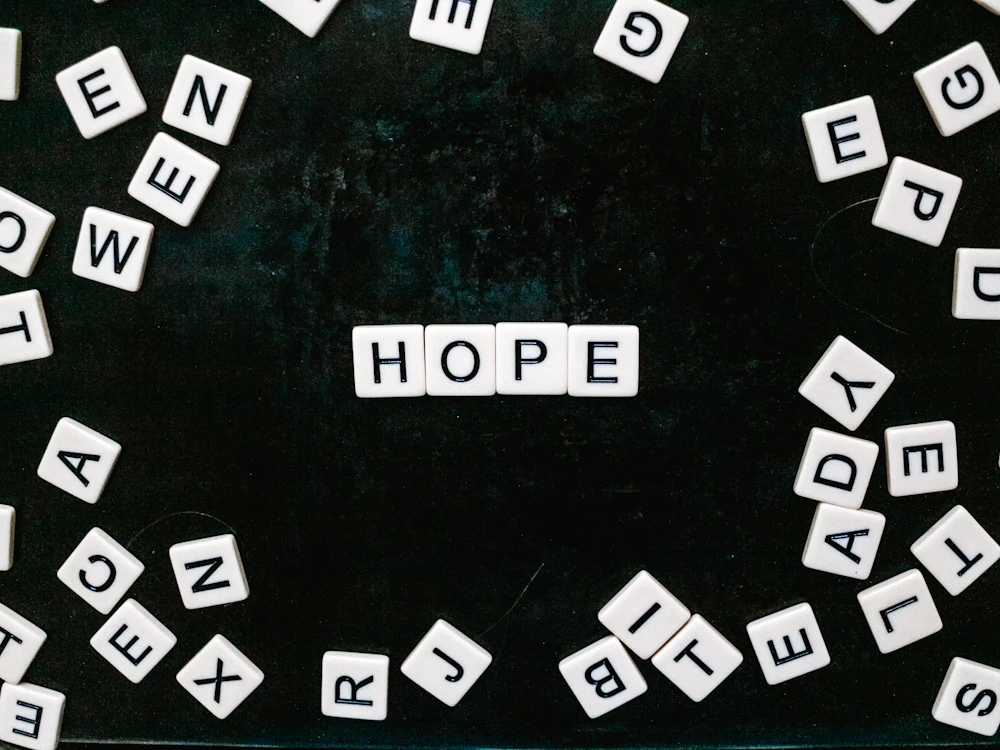 Scrabble tiles spelling HOPE, surrounded by loose letter tiles on a table