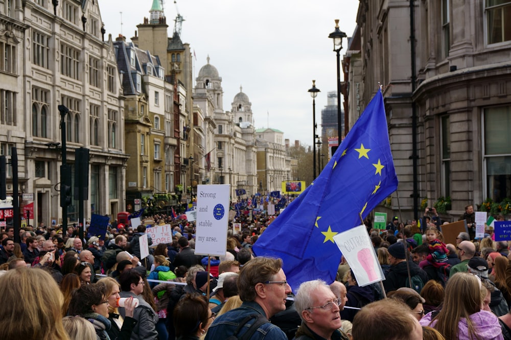 people lot near a blue flag and buildings during daytime
