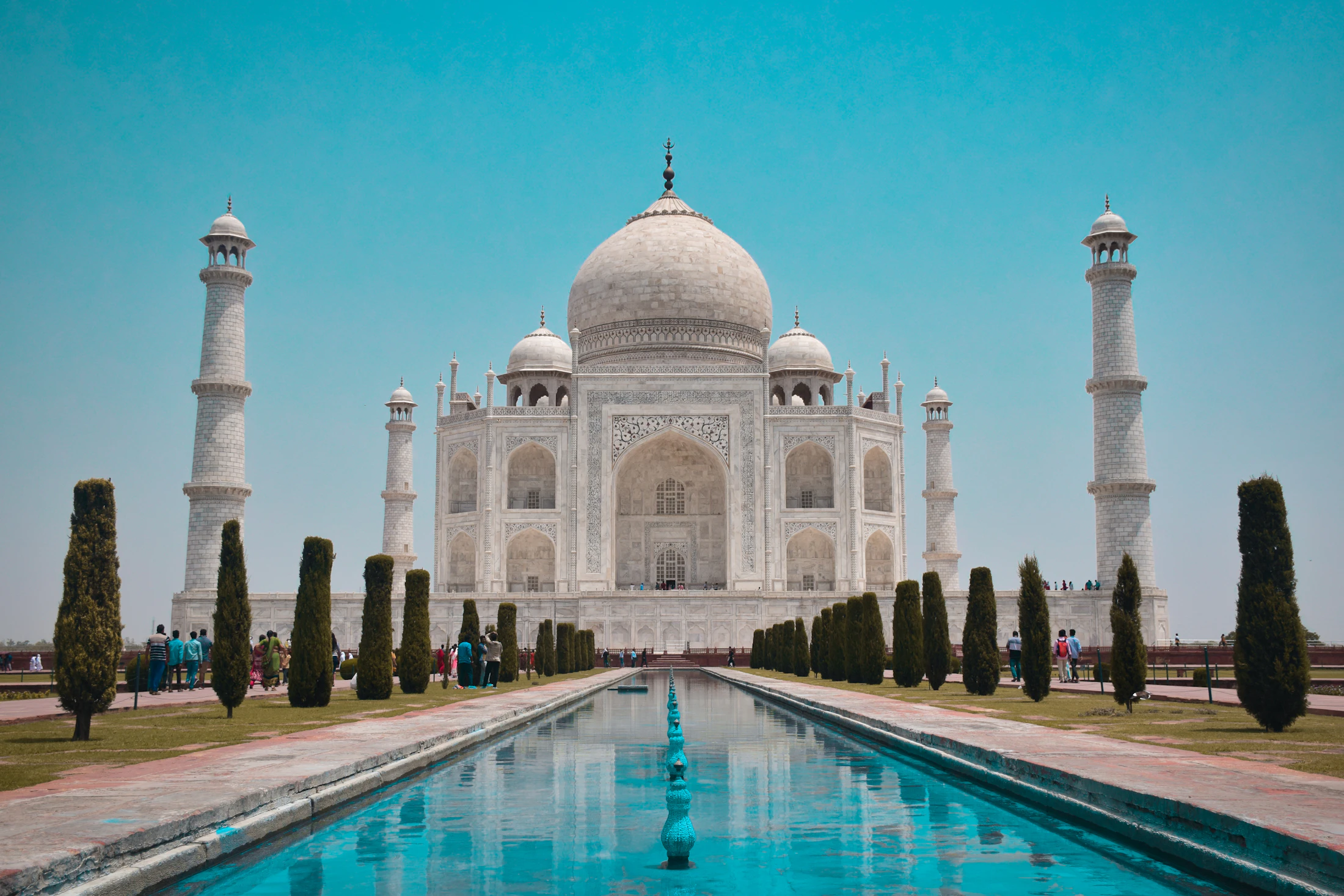 The Taj Mahal reflected in its long garden pool under a clear blue sky