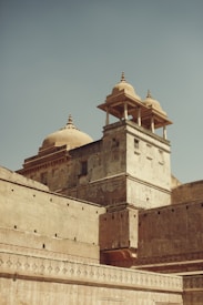 A historic building with intricate architectural details and domed towers, showcasing a blend of traditional design. The stone structure exhibits signs of weathering, adding to its antiquated charm. The image captures the grandeur and elegance of the architecture against a clear sky.