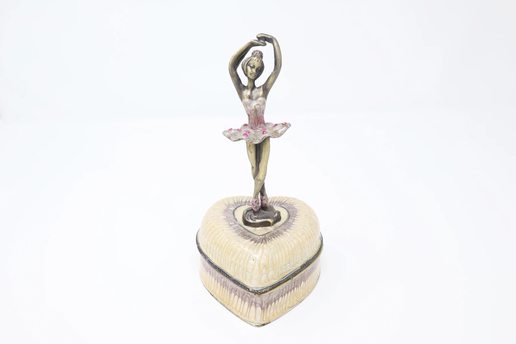 A small metal ballerina figure standing on a cream heart-shaped musical box against a white background