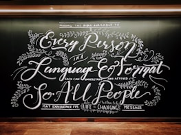 Intricate chalkboard art with elaborate, cursive text and decorative floral elements. The design emphasizes accessibility of messages across languages and formats.