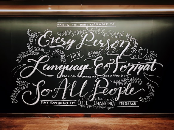 Intricate chalkboard art with elaborate, cursive text and decorative floral elements. The design emphasizes accessibility of messages across languages and formats.