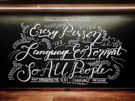 Intricate chalkboard art with elaborate, cursive text and decorative floral elements. The design emphasizes accessibility of messages across languages and formats.