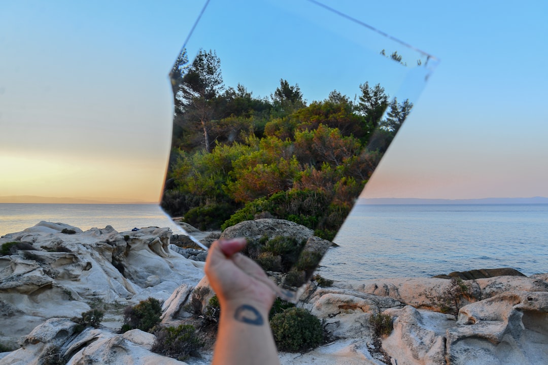 person holding mirror near ocean during daytime