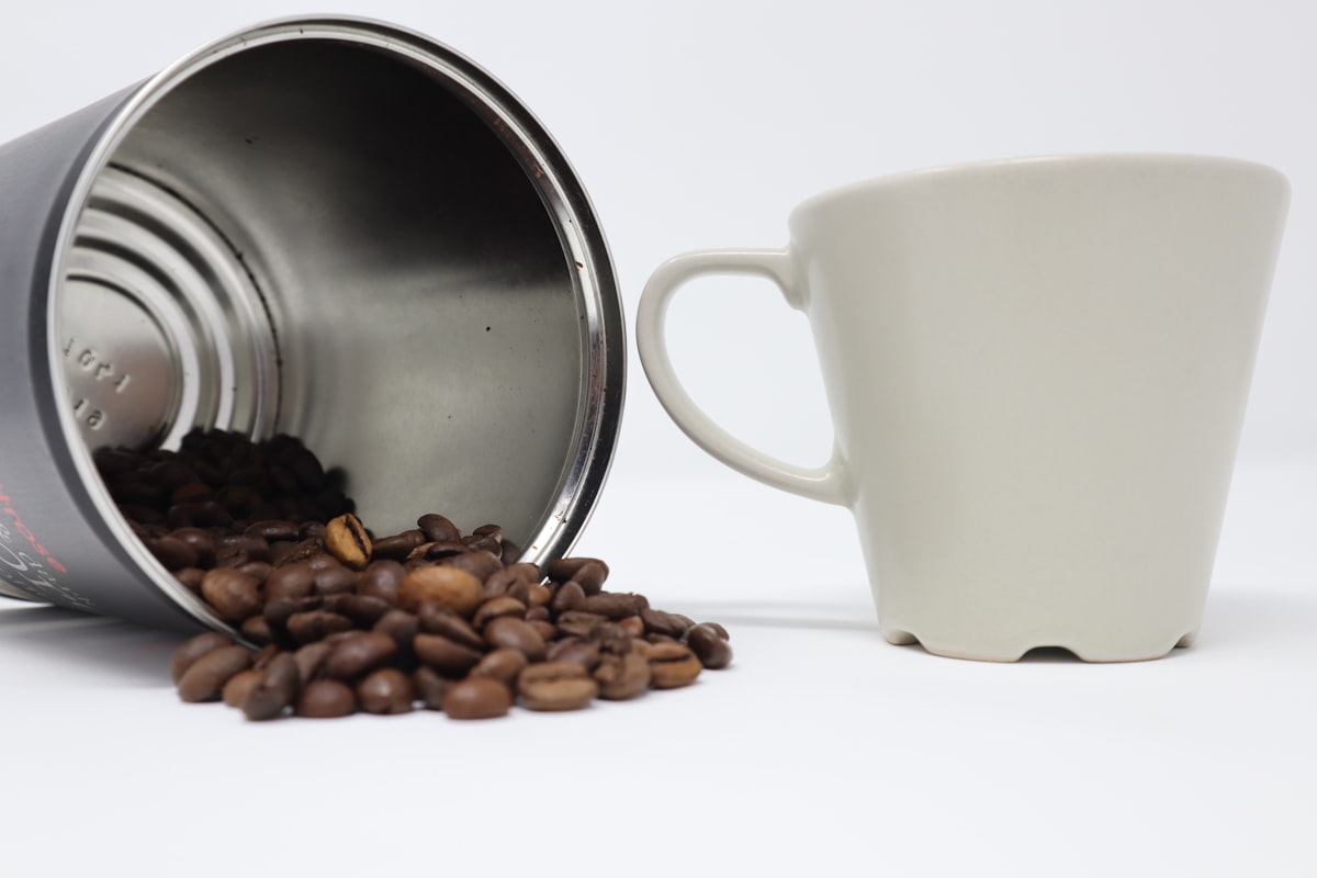 Black coffee beans surrounding a white ceramic mug of fresh coffee
