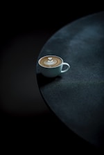 A vibrant photo of a spiced latte in a black cup with orange highlights on a dark table.