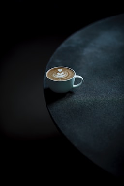 A vibrant photo of a spiced latte in a black cup with orange highlights on a dark table.