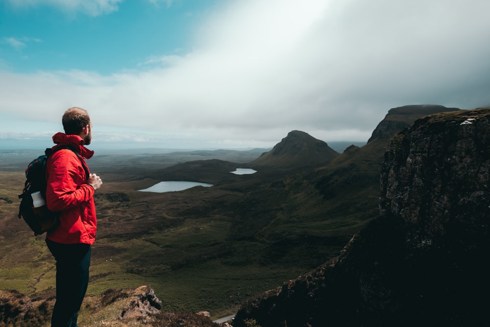 a man in a red jacket is standing on a hill