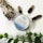 A tin of peppermint eucalyptus hemp soothing salve is placed on a white surface. Surrounding it are three dark crystals, a bundle of dried sage tied with string, and a sprig of green leaves.