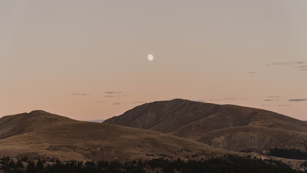 the moon is setting over a mountain range