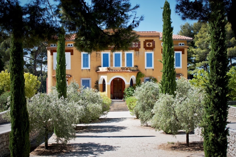 Casa de hormigón naranja y azul rodeada de árboles altos y verdes