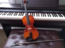 brown violin with brown violin bow beside white electronic keyboard