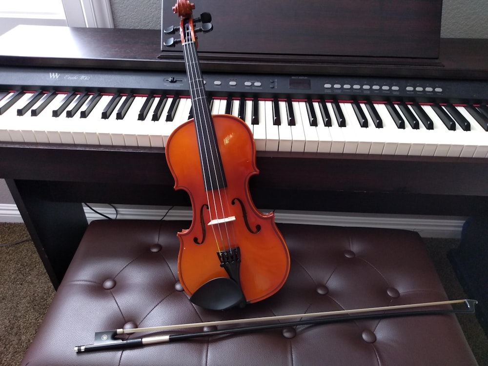 Violín marrón con arco de violín marrón junto a teclado electrónico blanco