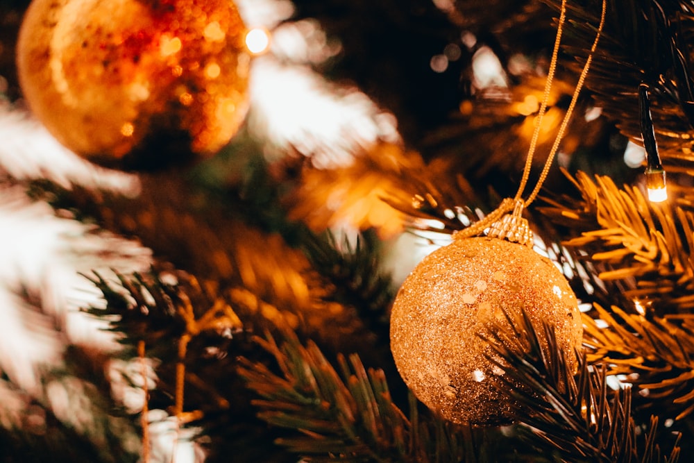 bokeh photography of gold Christmas bauble hanging from a tree