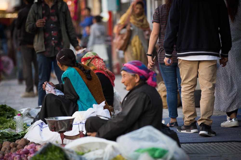 old woman sitting and selling goods on street near people walking