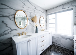 Bright marble and gold bathroom with two sinks and two mirrors.