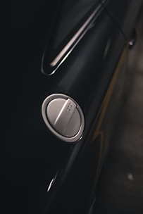 A close-up view of a car's fuel cap, set against a polished, dark-colored car body. The image captures the sleek design and metallic textures of the vehicle's exterior.