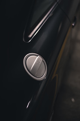 Close-up of a hand holding a mpg-caps capsule next to a car fuel tank, with a green and blue color scheme in the background.