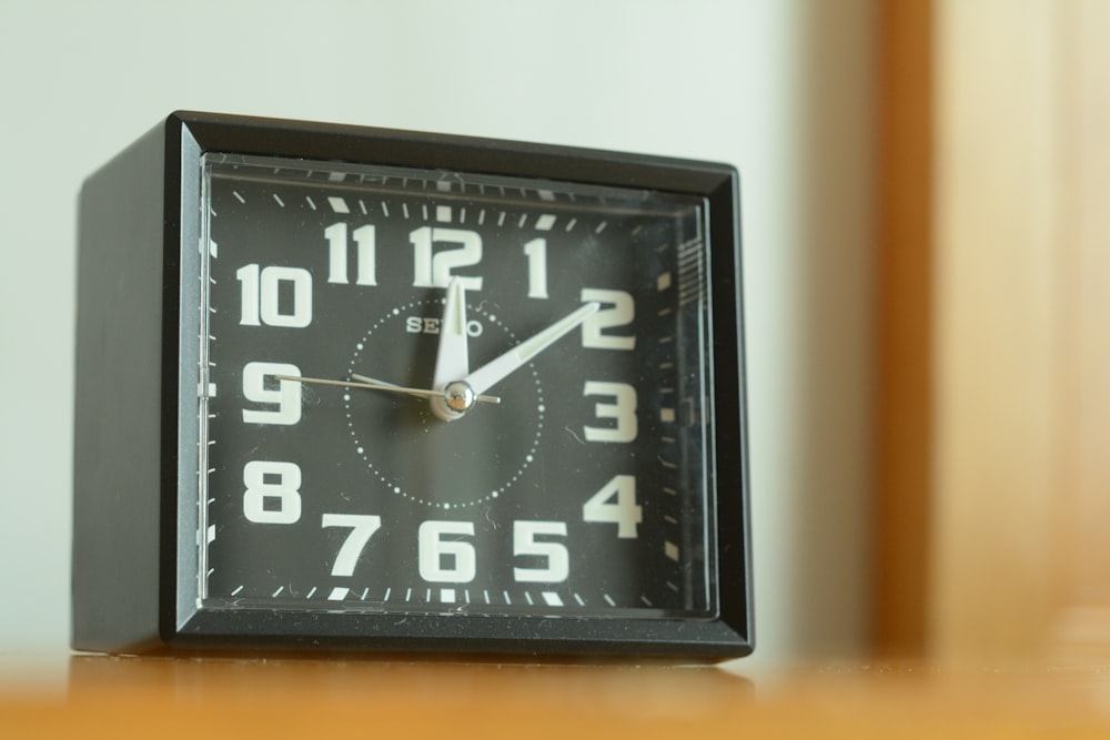 square black analog desk clock 12:05 o'clock