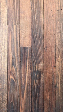 Dark wooden planks with visible grain patterns and some knots create a rustic and textured surface. The wood has various shades of brown, ranging from light to dark tones, adding depth and character.