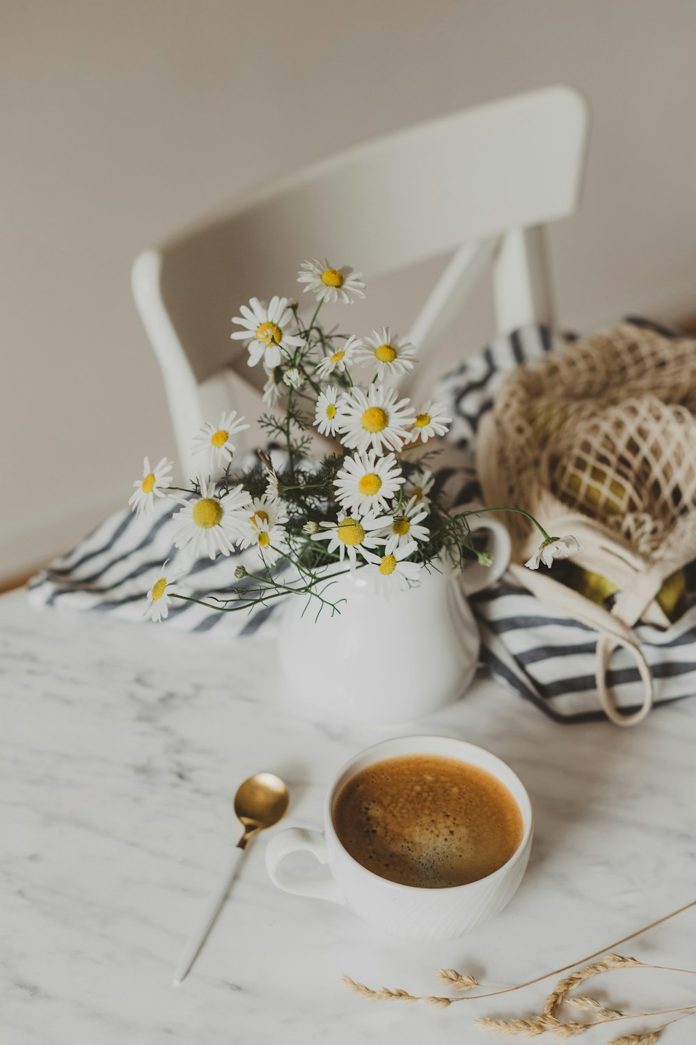 cappuccino near white and yellow flowers in vase on white table