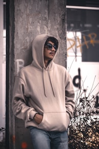 men wearing a grey hoodie jacket leaning in a wall during daytime