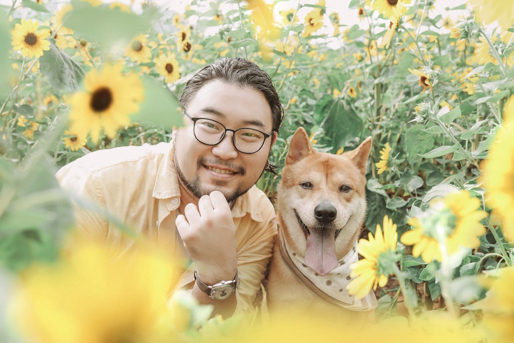 낮에 해바라기 밭 근처에서 갈색 개 옆에서 웃고 있는 사진