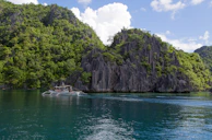 A traditional Filipino boat sailing under a bright blue sky near the limestone cliffs of El Nido.
