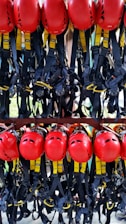 A collection of bright red helmets and black harnesses with yellow accents are neatly organized and hanging on a rack. They are likely used for safety in activities such as climbing or construction.