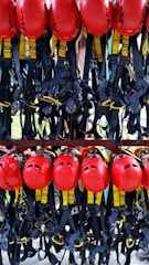 A collection of bright red helmets and black harnesses with yellow accents are neatly organized and hanging on a rack. They are likely used for safety in activities such as climbing or construction.